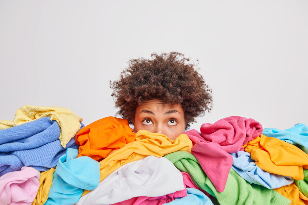a woman hiding behind a pile of clothes