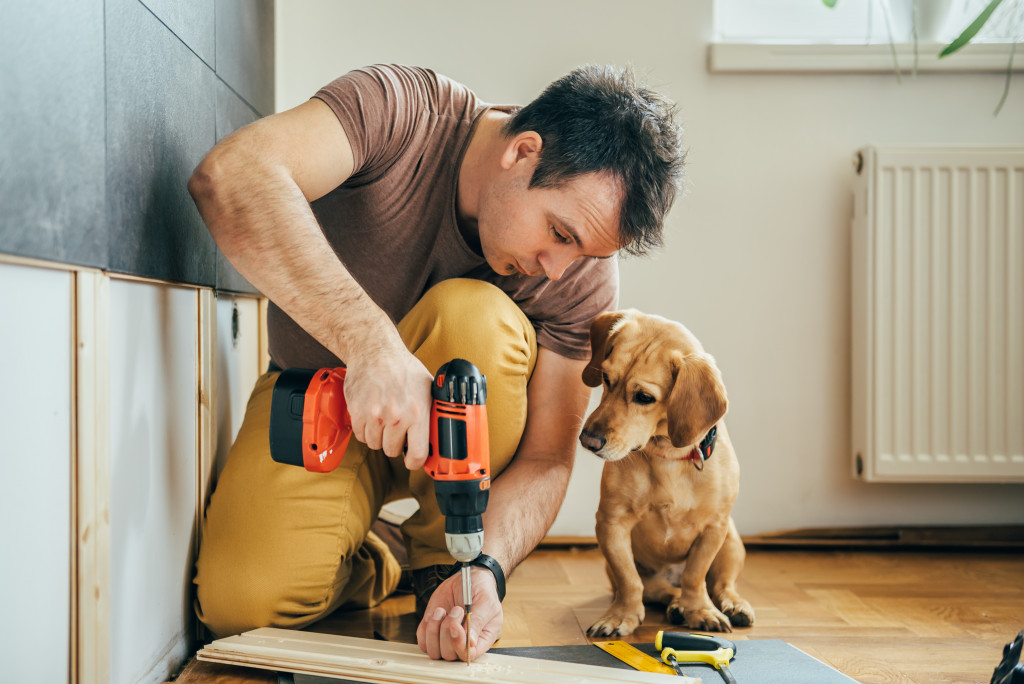 A builder using a drill indoor while a cute dog watches