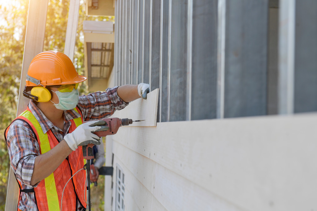 a man in a safety gear drilling a siding to a home